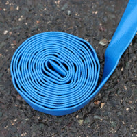 A bright blue 25mm layflat hose, coiled into a roll on dark asphalt pavement.