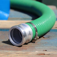 A green heavy duty garden hose with a silver metal cam adapter and hose clip, resting on a wooden surface.