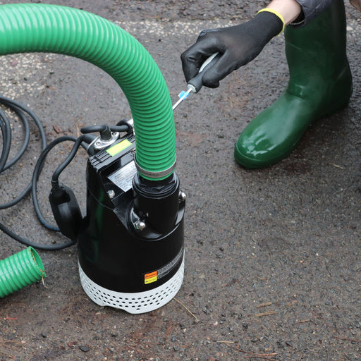 Person using a submersible pump with a green 50mm hose on a concrete surface

