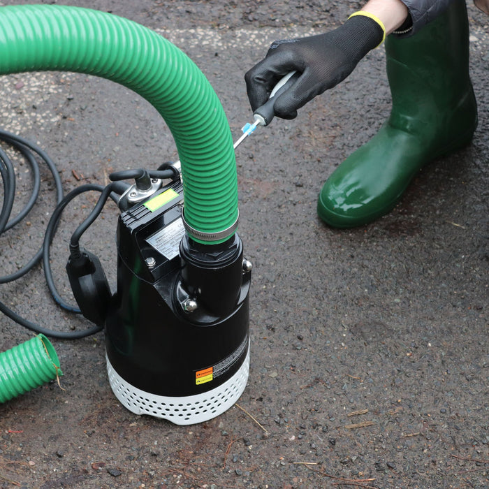 Person using a submersible pump with a green 50mm hose on a concrete surface

