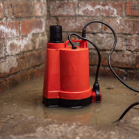 APP BPS manual puddle pump standing in shallow water against a brick wall background.
