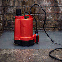 automatic submersible water pump with float switch sitting on wet stone flooring against a brick wall background