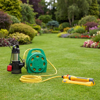 A garden hose reel system on a green lawn, featuring a black and silver submersible pump, a green hose reel, a yellow coiled hose, and a yellow spray nozzle, with a blurred garden background.