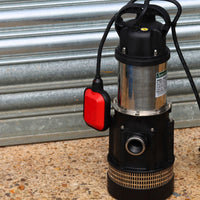 Submersible well pump with red float switch on a concrete floor against a metal wall.