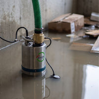 Evak residox submersible pump with a green hose pipe attached at the top, standing in shallow water in a basement. The pump has a visible Evak logo on the front.