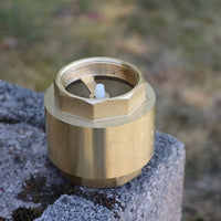 32mm brass non-return value for water pump, resting on a grey stone against a blurred outdoor background.