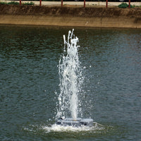 A floating fountain pump and nozzle system in a pond, actively spraying water high into the air with ripples on the surface.