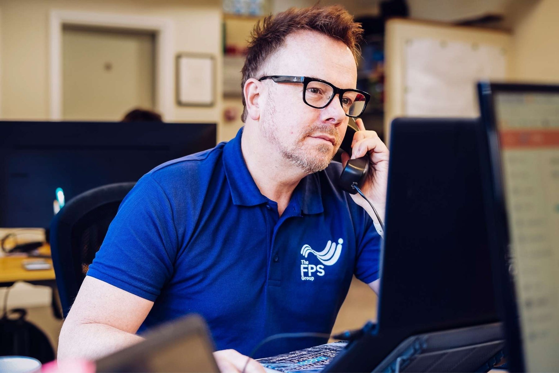 Man in blue shirt with FPS logo on phone call in office setting