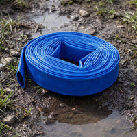 A bright blue coiled layflat hose on muddy ground with puddles and small patches of grass visible.