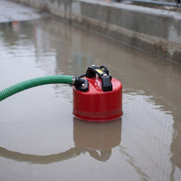 A red submersible puddle pump with a green hose attached, floating in dirty water.