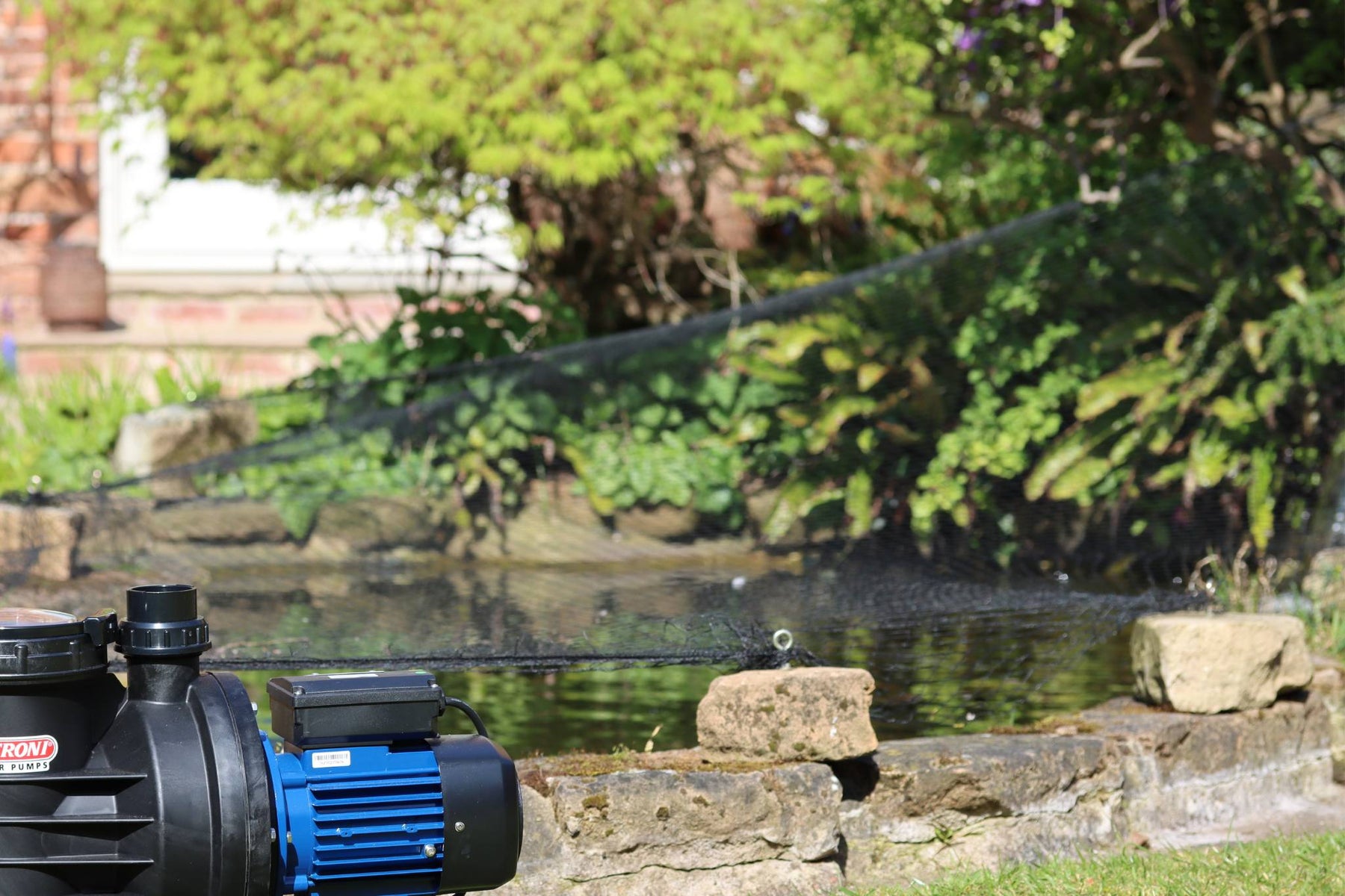 Pond pump with blue motor on a stone ledge by a pond