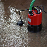 A submersible water pump with a red and black body, a green hose, and a power cord, shown operating in shallow water.