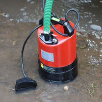 submersible puddle pump with a green flexible hose pipe, shown standing in shallow water outdoors.