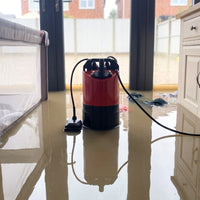 automatic puddle pump standing on a flooded floor in a home near large patio doors.