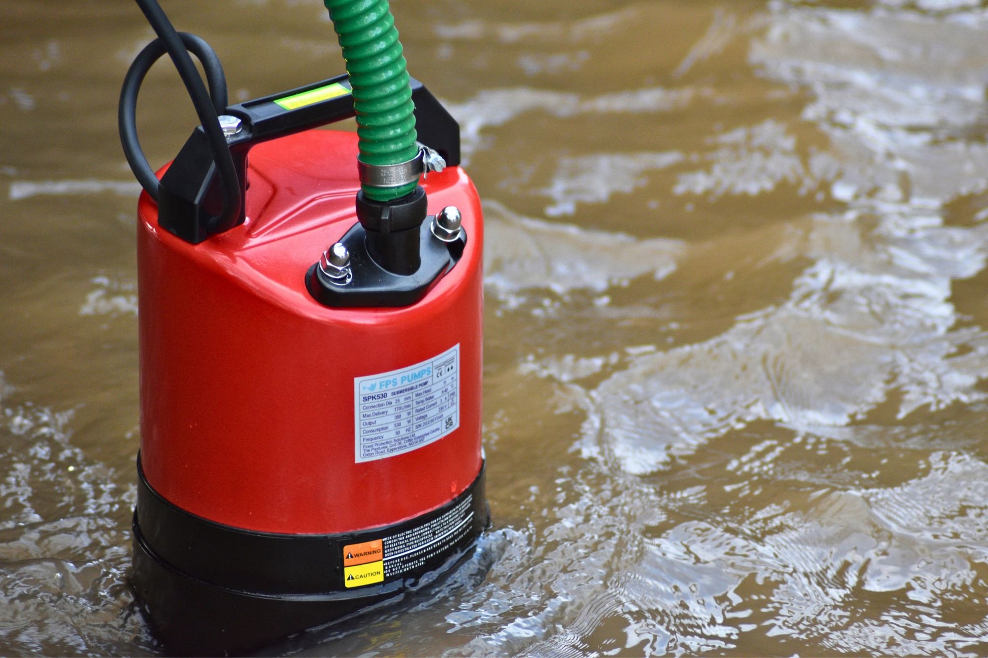 Red submersible pump with a green hose in floodwaters

