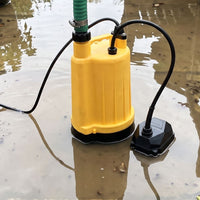 A yellow submersible puddle pump with a green hose, shown partially submerged in shallow muddy water