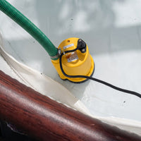 A yellow submersible puddle pump with a green hose and black power cord, shown installed inside a hot tub