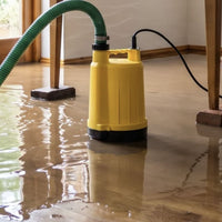 A SPP2 puddle pump with a green suction and delivery hose, shown clearing water from a small flood in a home