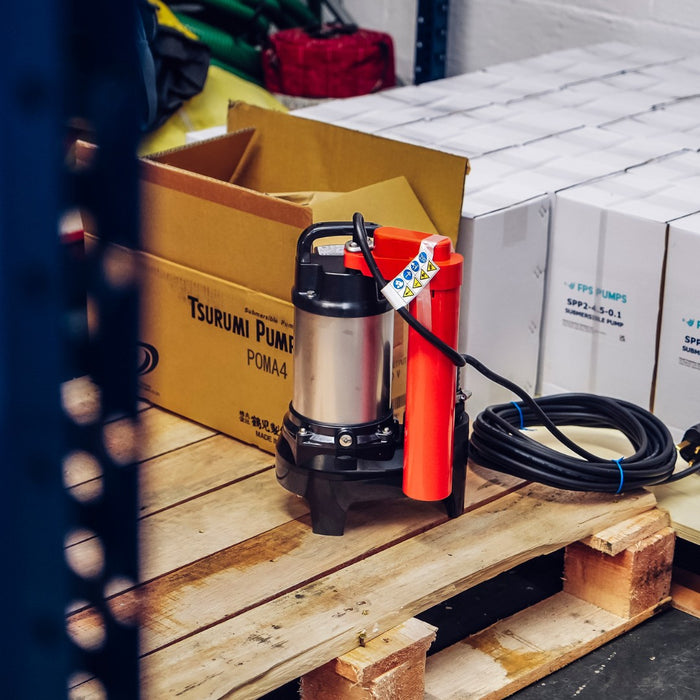 Tsurumi POMA Pump in warehouse with orange tube float switch, ideal automatic submersible pump for narrow chambers, pictured in front of stocked puddle pumps on a wooden pallet at the Flood & Water Pumps warehouse.