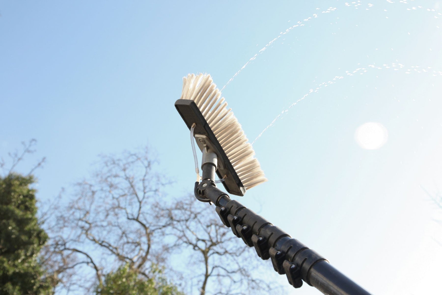 Telescopic cleaning brush with a long handle against a clear blue sky with water pump