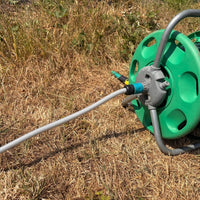 A green plastic hose reel with a 13mm clear braided hose pipe  connected, photographed outdoors on dry grass.