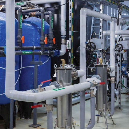 Industrial plumbing system with pipes, valves, and blue tanks in a mechanical room.