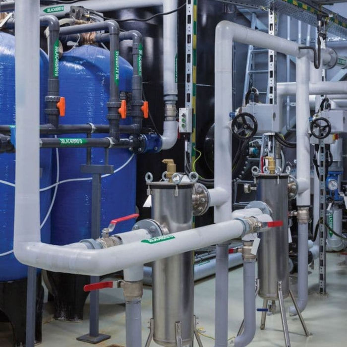 Industrial plumbing system with pipes, valves, and blue tanks in a mechanical room.